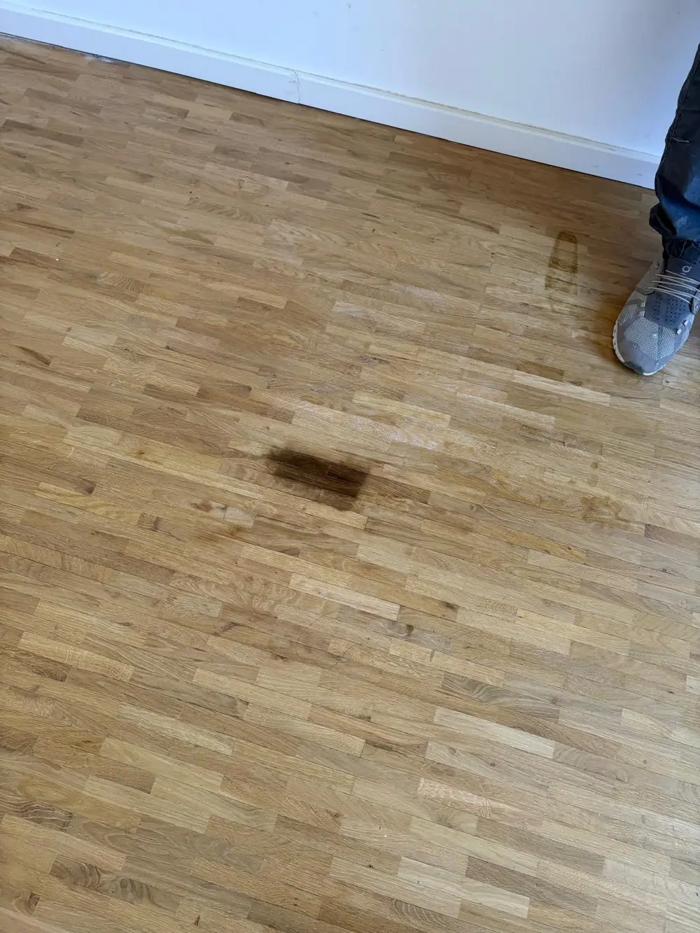 Nahaufnahme eines Parkettbodens mit einer dunklen, rechteckigen Schadstelle und Gebrauchsspuren.