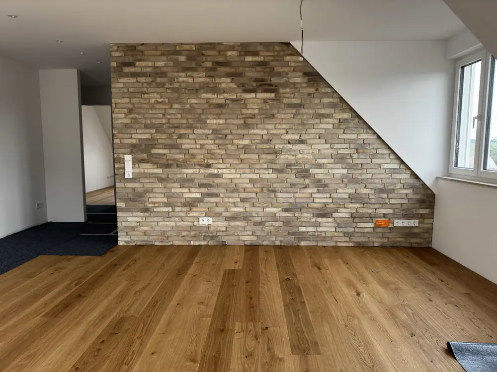 Heller Holzboden in einem Wohnraum vor einer großflächigen Wand mit strukturierter Steinoptik und schrägem Wandverlauf.