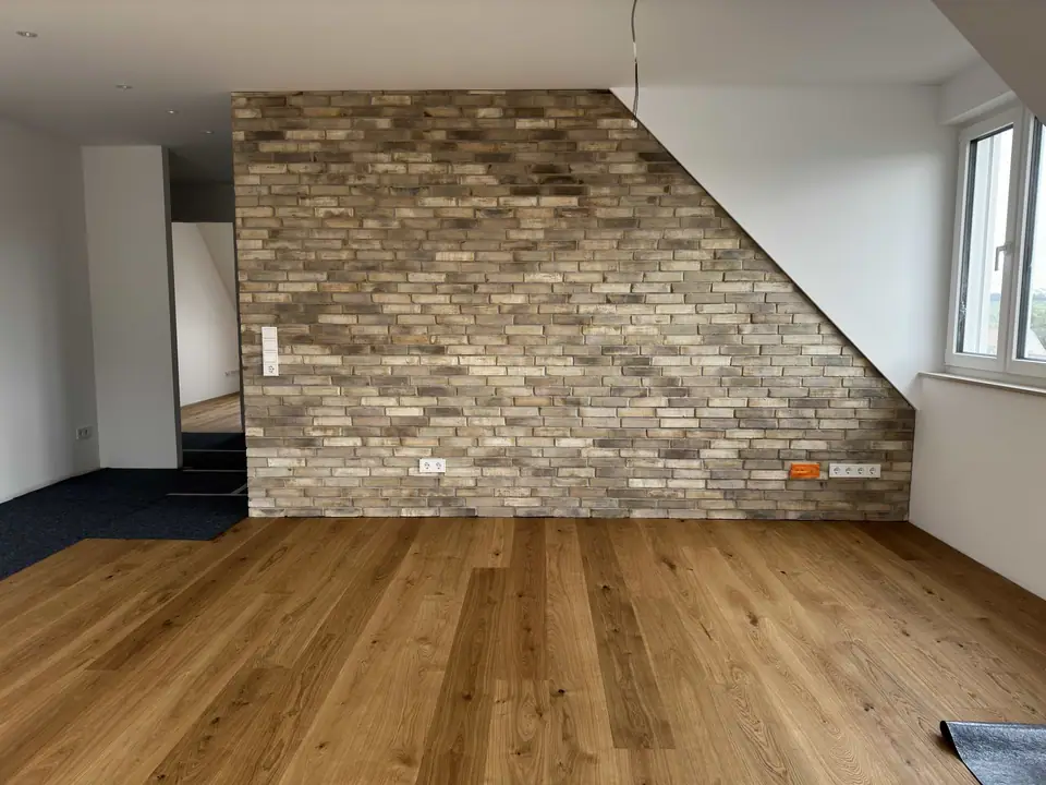Heller Holzboden in einem Wohnraum vor einer großflächigen Wand mit strukturierter Steinoptik und schrägem Wandverlauf.
