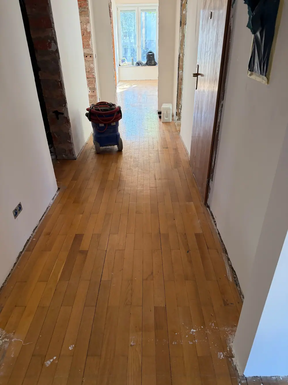 Blick durch einen Flur mit längs verlegtem Holzboden; ein Baugerät steht mittig auf der Fläche.