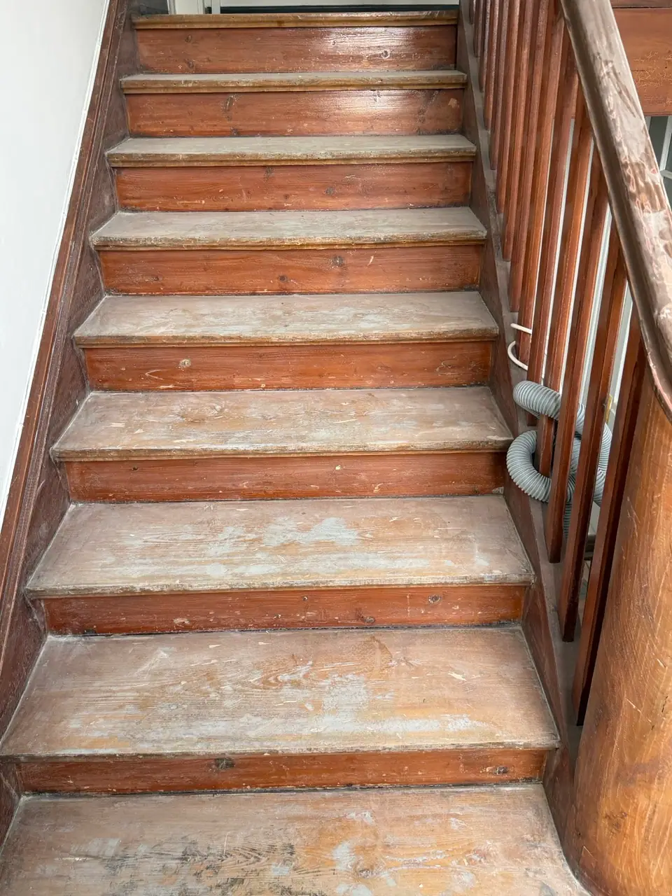 Blick von unten auf eine stark beanspruchte Holztreppe mit abgeriebenen und staubigen Trittflächen sowie Holzgeländer.