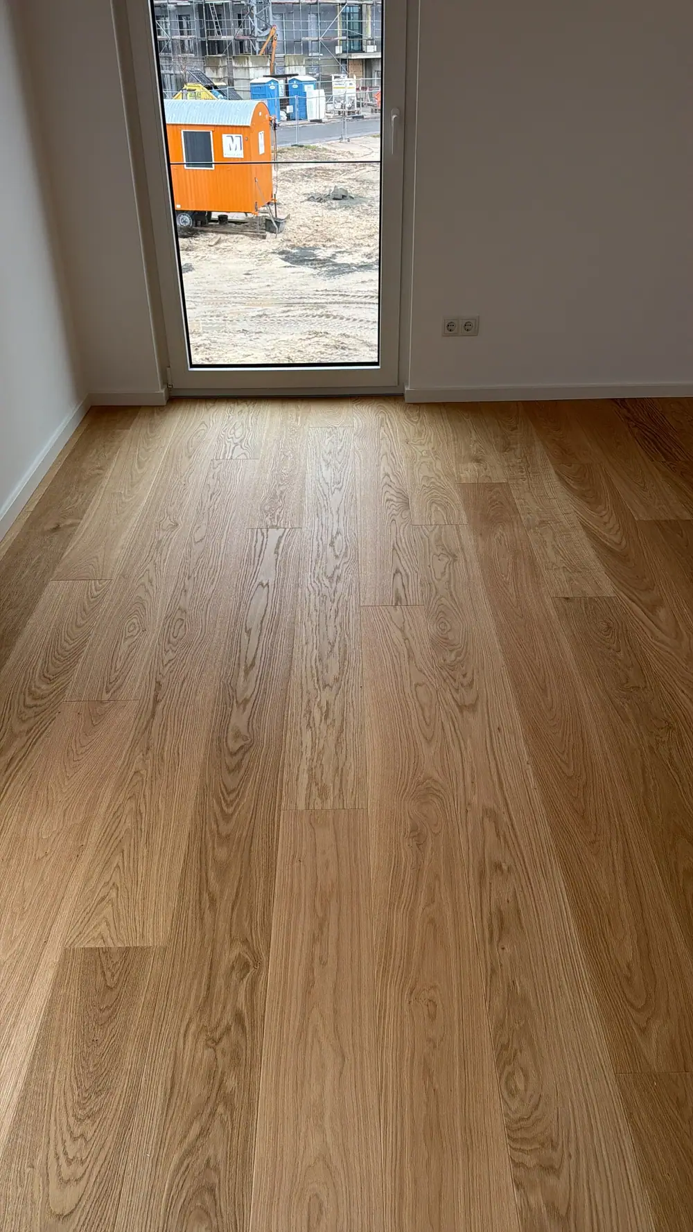 Blick auf verlegte Eiche-Landhausdielen in einem hellen Raum vor einer bodentiefen Fenstertür.