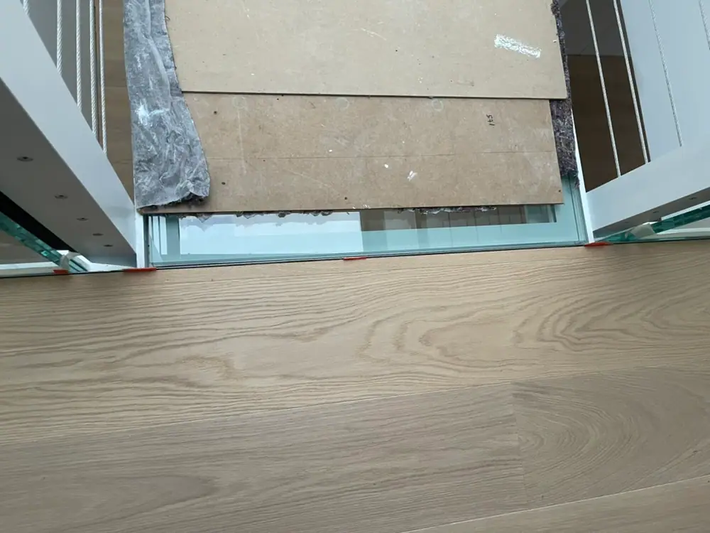 Helle Eichenholzdielen an einer Glasbrüstung neben einem Treppenbereich während der Arbeiten.
