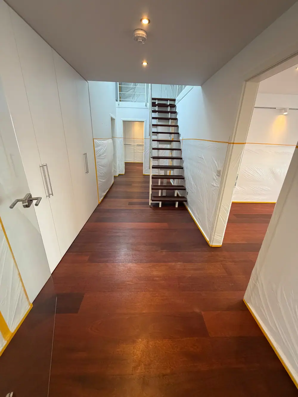 Flur mit dunklem Landhausdielenparkett, weißer offener Treppe und abgedeckten Wandflächen.
