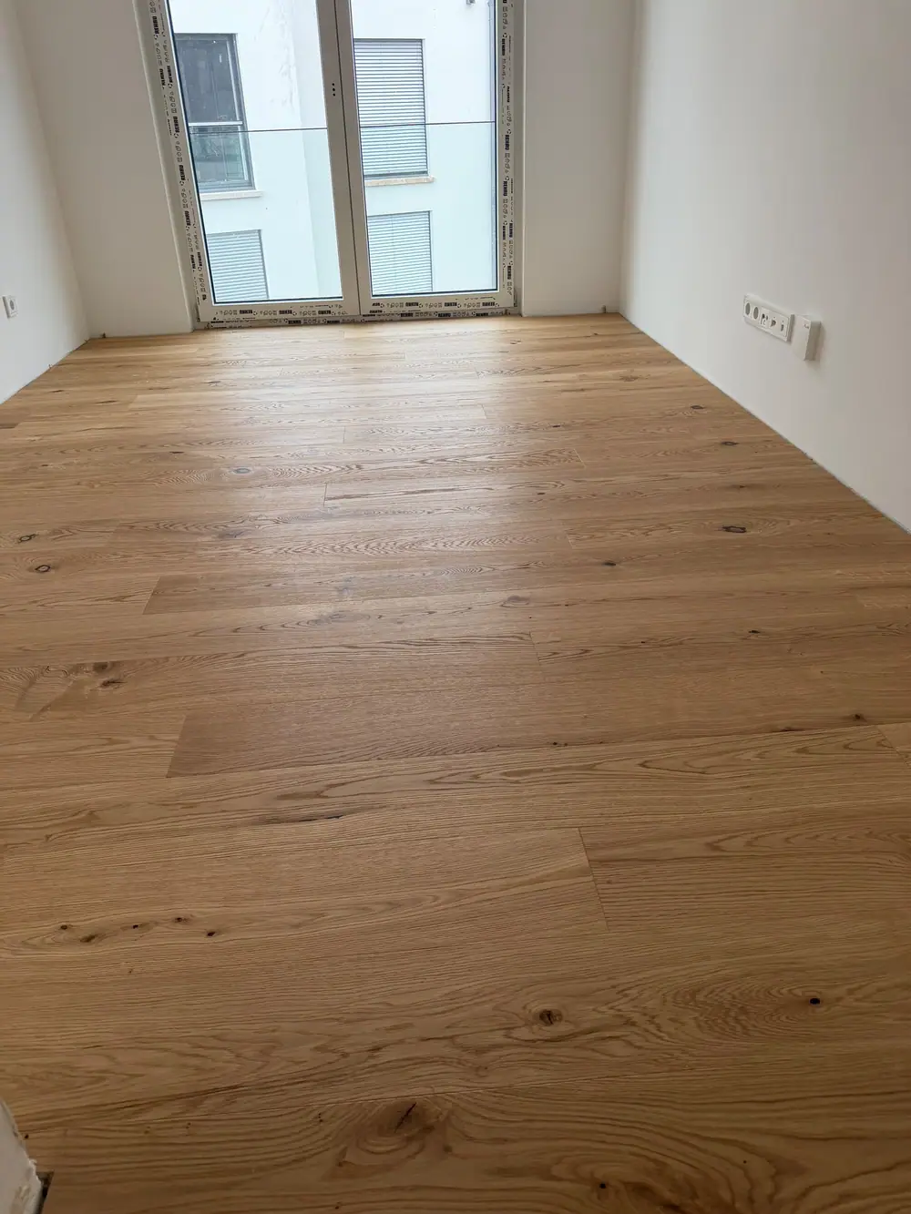 Raumansicht mit großflächig verlegten Eichen-Landhausdielen vor einer bodentiefen Fensterfront.