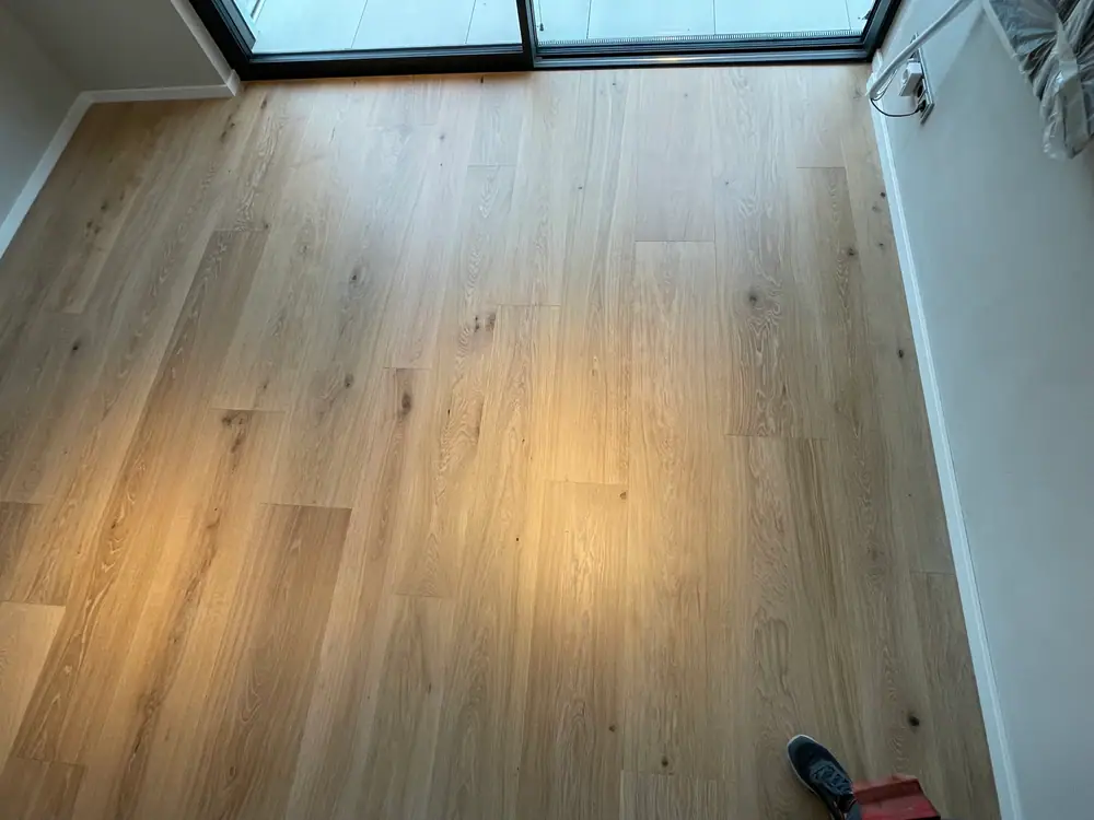 Heller Eichenboden mit sichtbaren Ästen vor einer bodentiefen Fensterfront mit dunklem Rahmen.