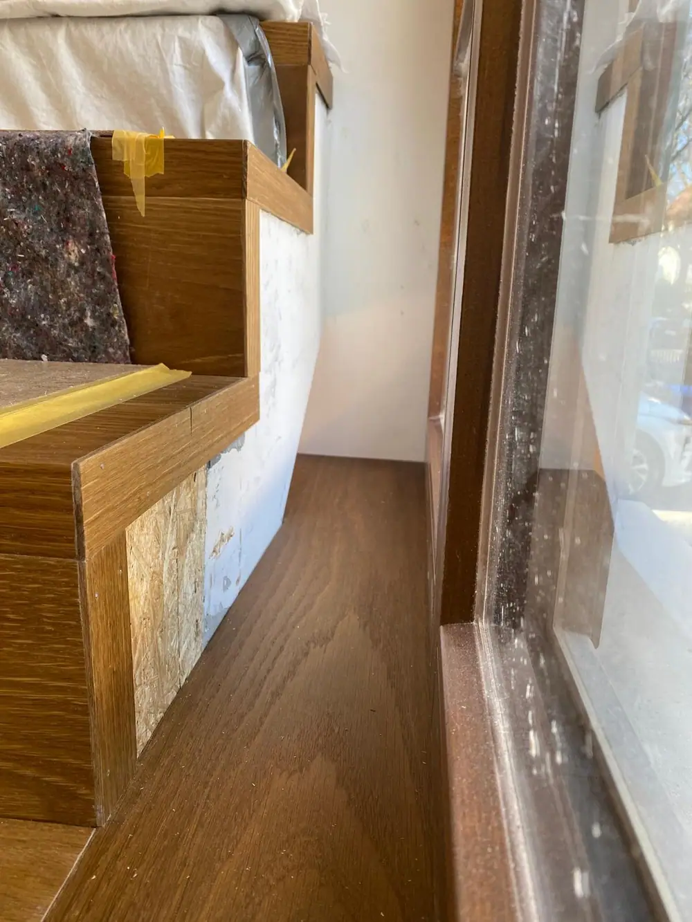 Seitliche Ansicht einer mit Holz verkleideten Treppe neben einem Fenster; die Holzfläche läuft bis an die Fensterbank.