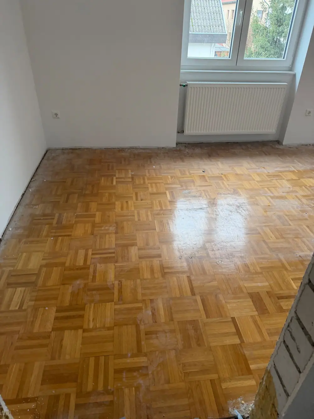 Älteres Eiche-Mosaikparkett mit sichtbaren Gebrauchsspuren und unterschiedlich glänzenden Bereichen vor der Sanierung.