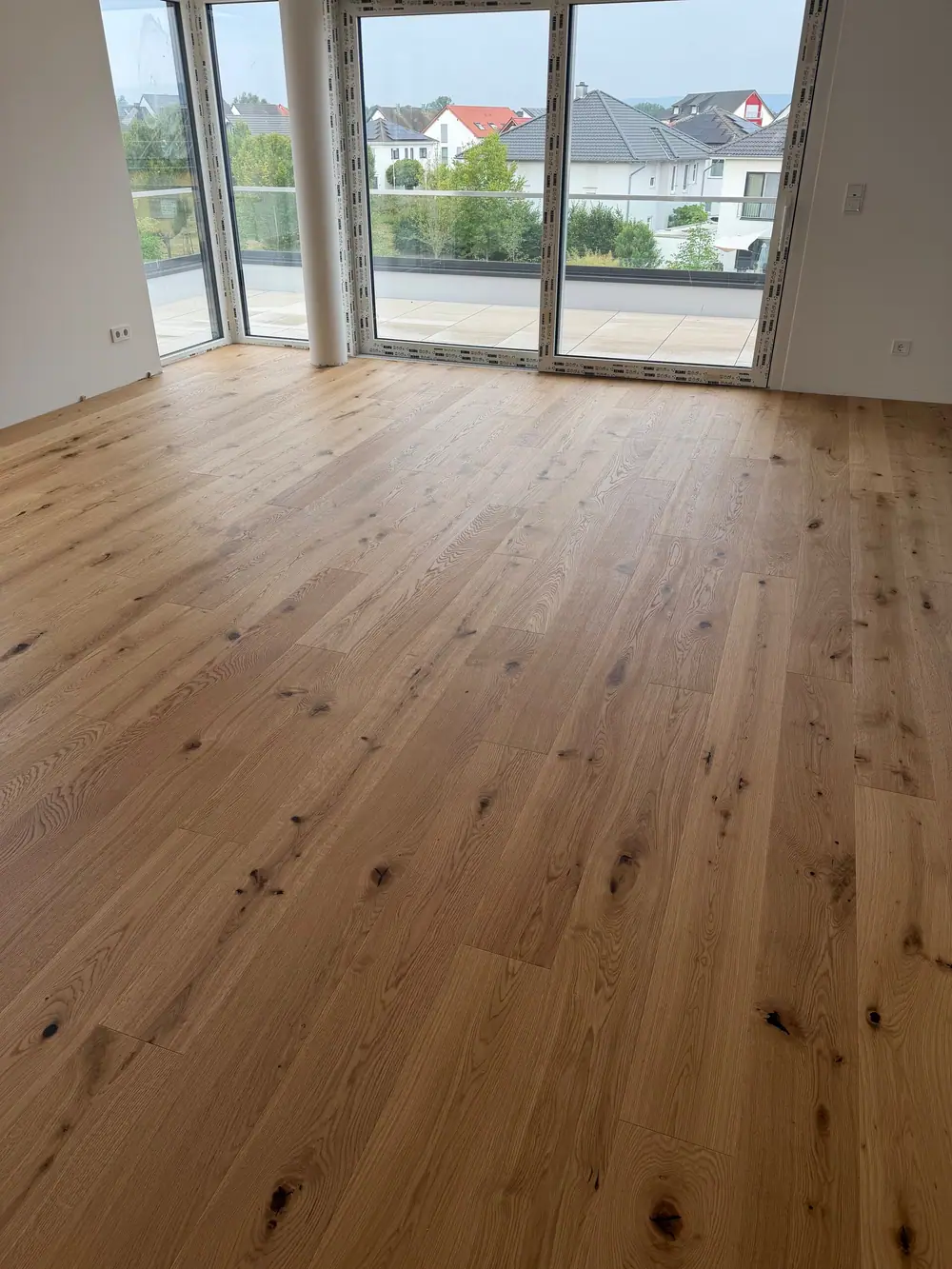 Heller Raum mit Eichen-Landhausdielen, runder Säule und großen Fenstern zur Terrasse.