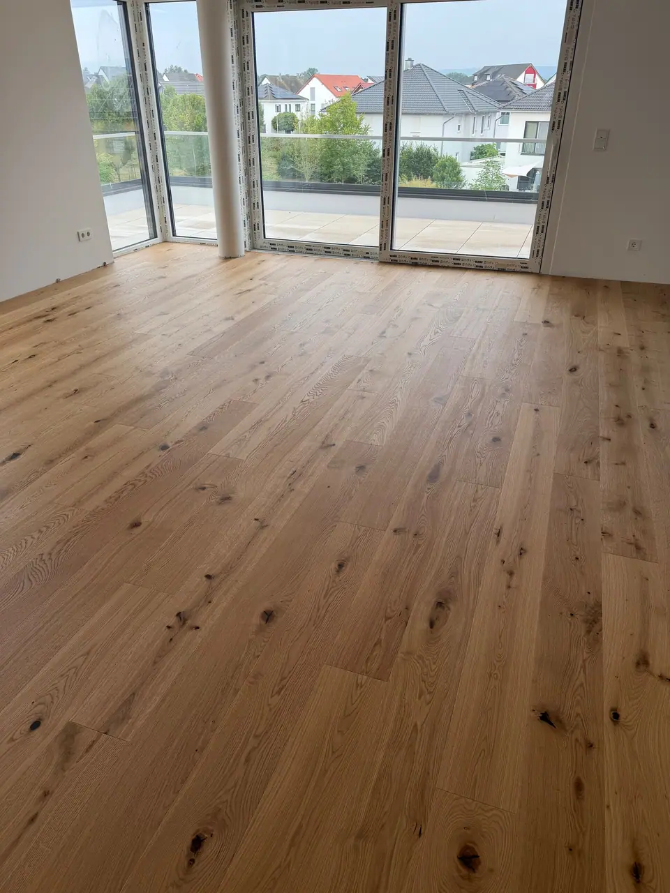 Heller Raum mit Eichen-Landhausdielen, runder Säule und großen Fenstern zur Terrasse.