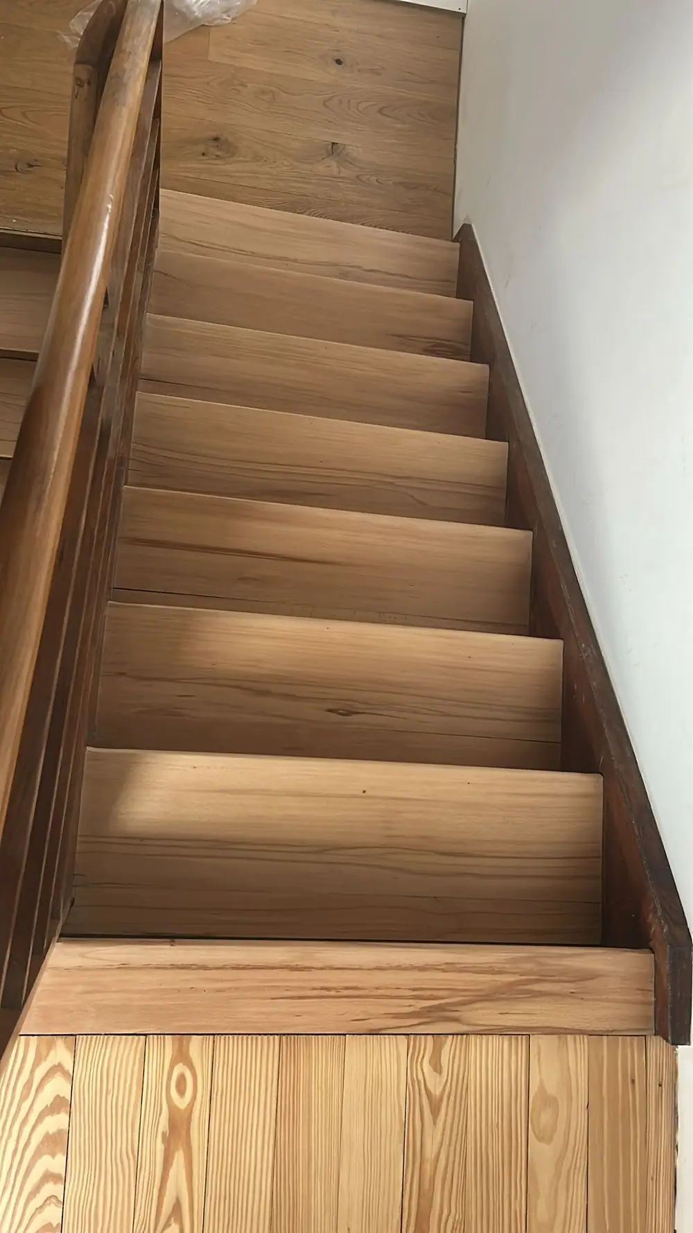 Holztreppe von unten mit sichtbaren Stufen, dunklem Geländer und weißer Wand.