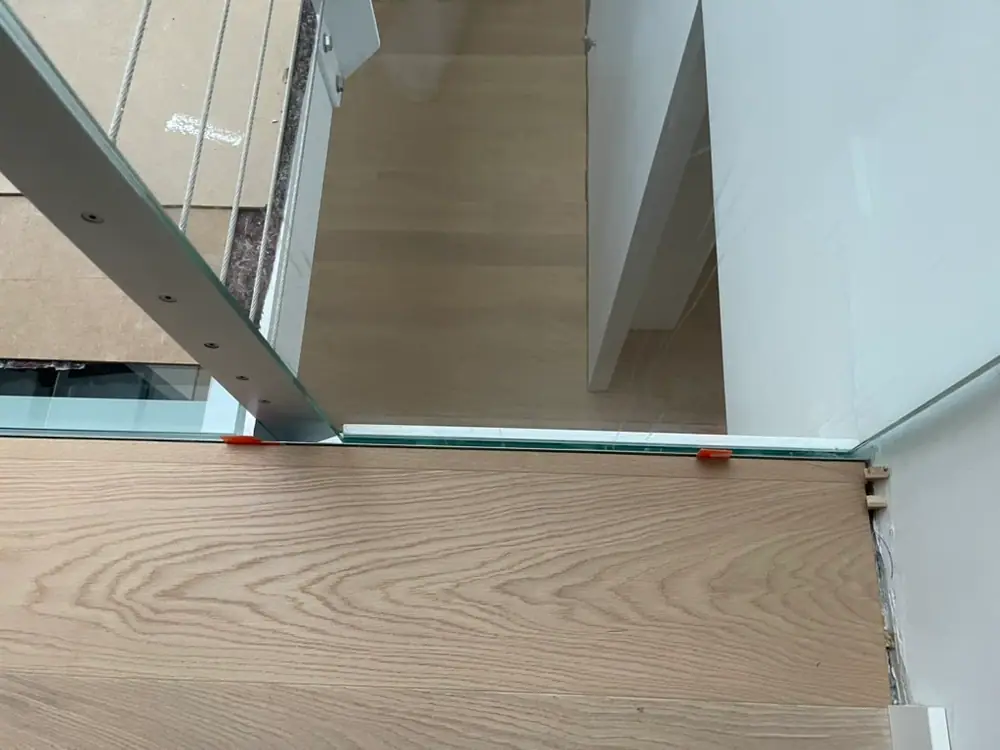Helle Dielenfläche mit Anschluss an Glasgeländer und weißer Wand am Treppenauge.