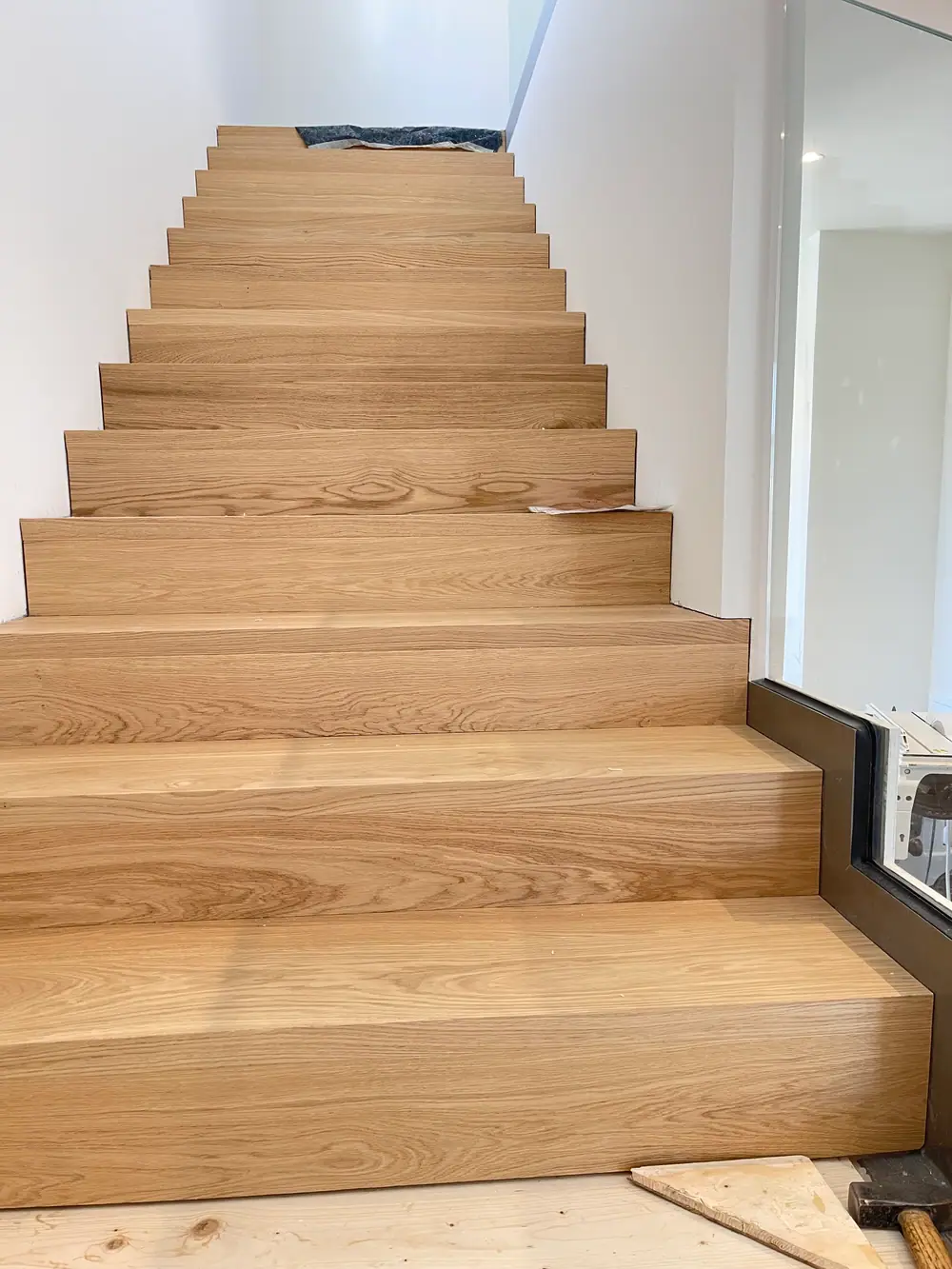 Treppe mit breiten Holzstufen und Glasgeländer während der Ausführung.