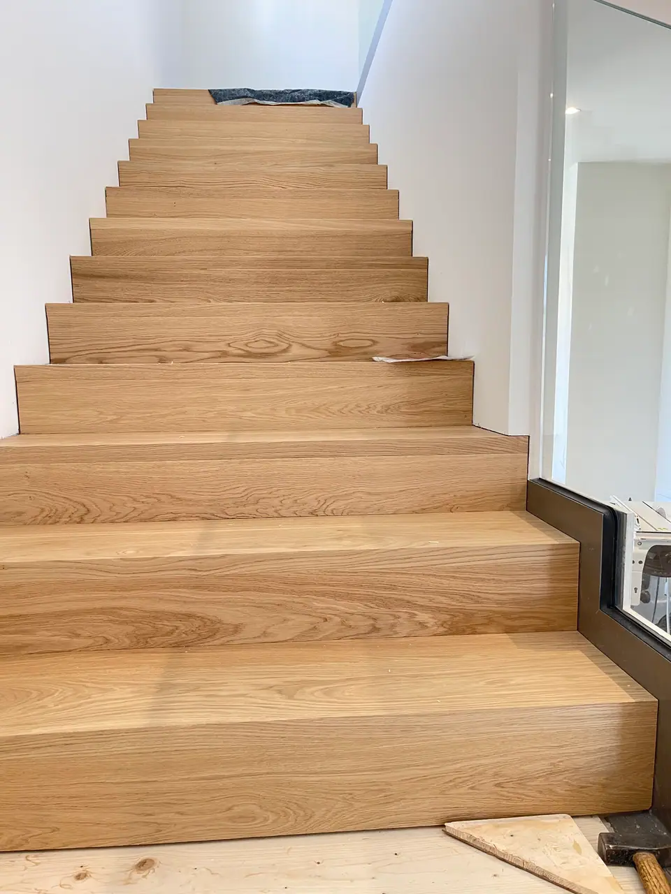 Treppe mit breiten Holzstufen und Glasgeländer während der Ausführung.