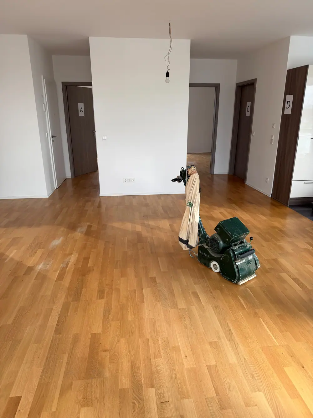 Großer Raum mit Eiche-Parkett und einer Schleifmaschine auf dem Boden.