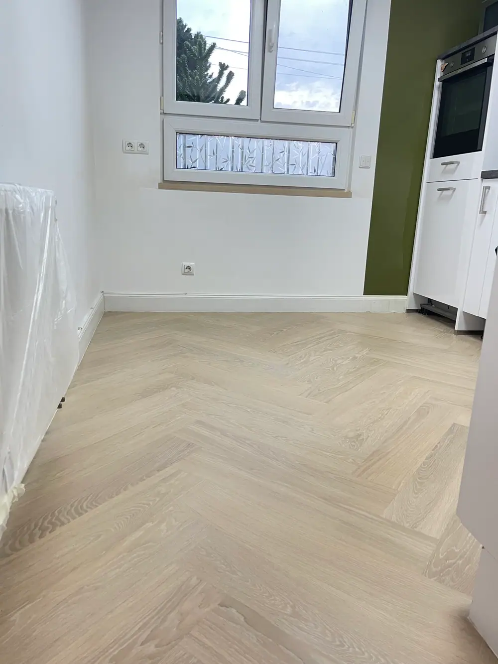 Helle Fischgrätefläche aus Eiche in einer Küche mit weißer Fensterfront, grüner Wandnische und weißen Küchenmöbeln.