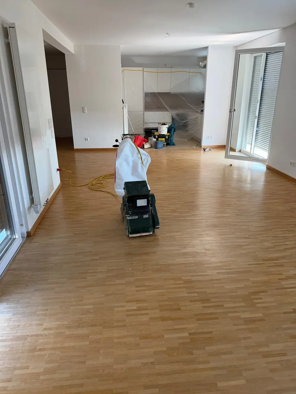 Großer Raum mit Eichenparkett, Schleifmaschine und abgehangenen Folien zum Schutz des angrenzenden Bereichs.