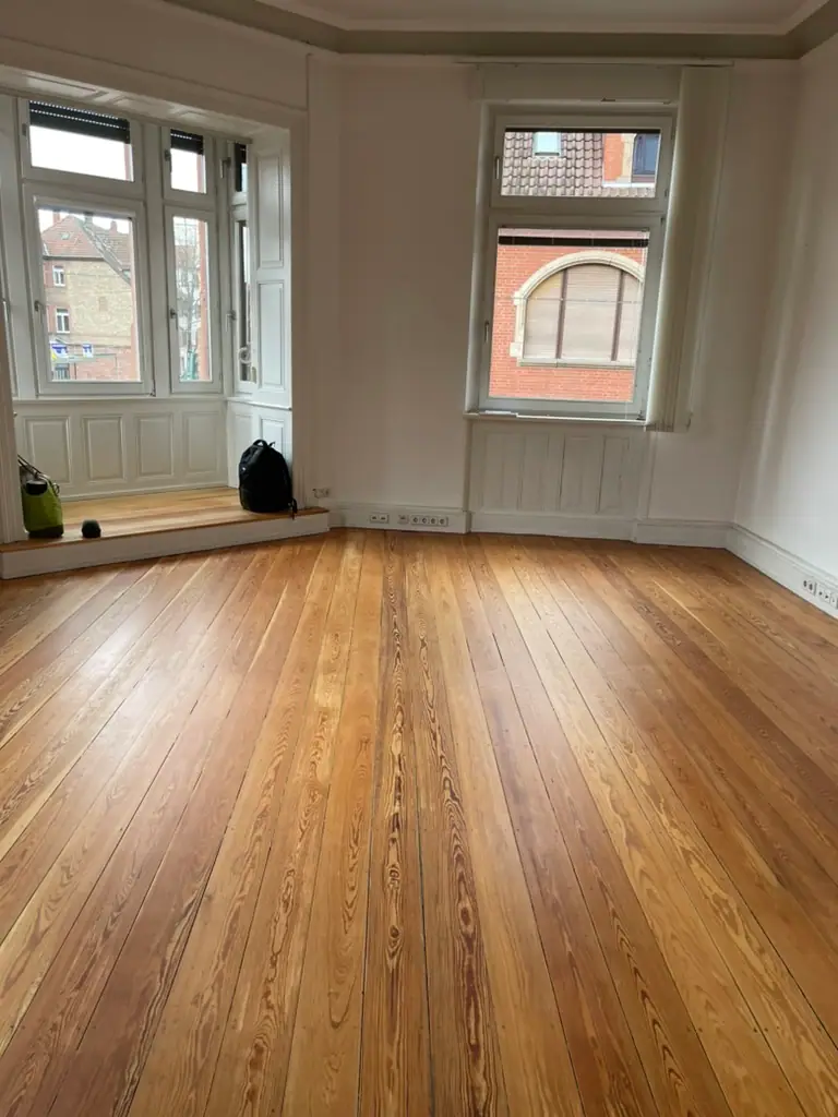 Heller Raum mit Erkerfenster und langen Holzdielen, deren markante Maserung zur Fensterfront verläuft.