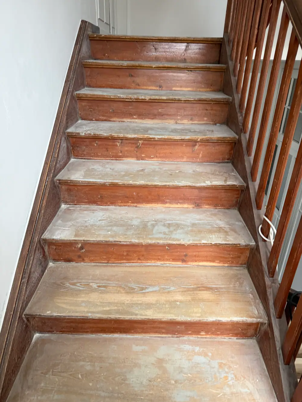 Seitlicher Blick entlang eines Treppenlaufs mit dunklen Holzstufen, Holzgeländer und sichtbaren Nutzungsspuren.