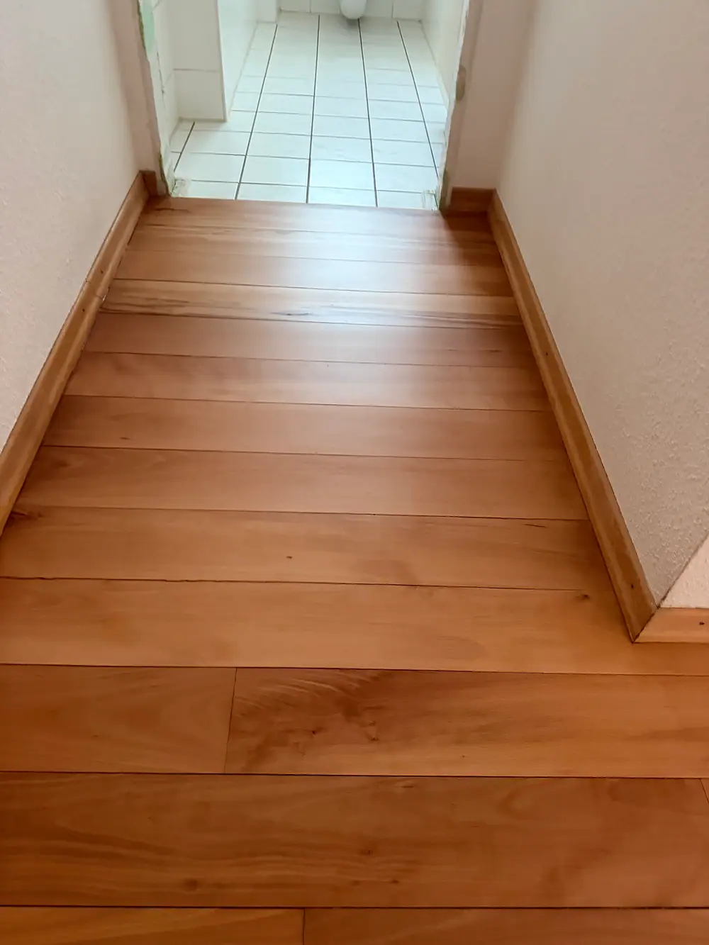 Blick auf eine Treppe mit hölzernen Stufen und angrenzendem Eichenparkett im Fischgrätmuster.