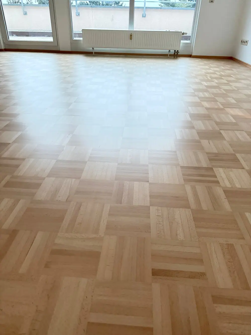 Weitläufige Ansicht eines hellen Raums mit matt versiegeltem Buchen-Mosaikparkett, Fensterfront und Heizkörper.