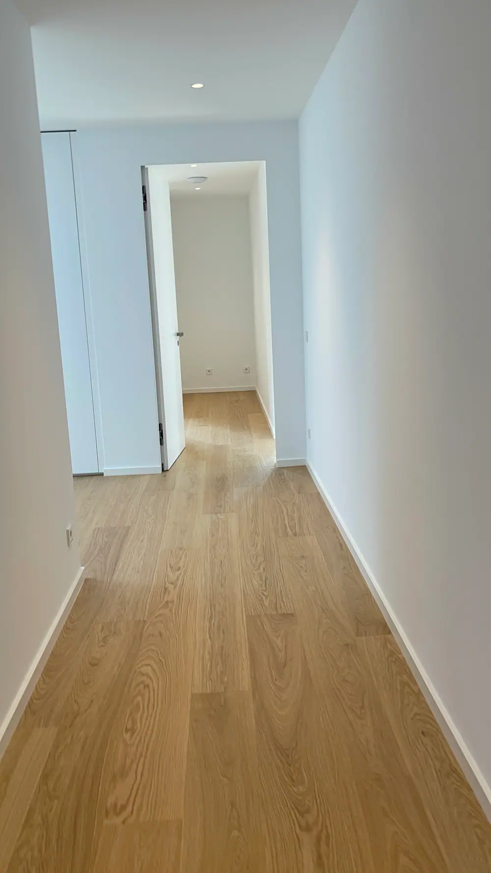 Schmaler weißer Flur mit hellem Dielenboden, offenen Türen und weißen Sockelleisten.