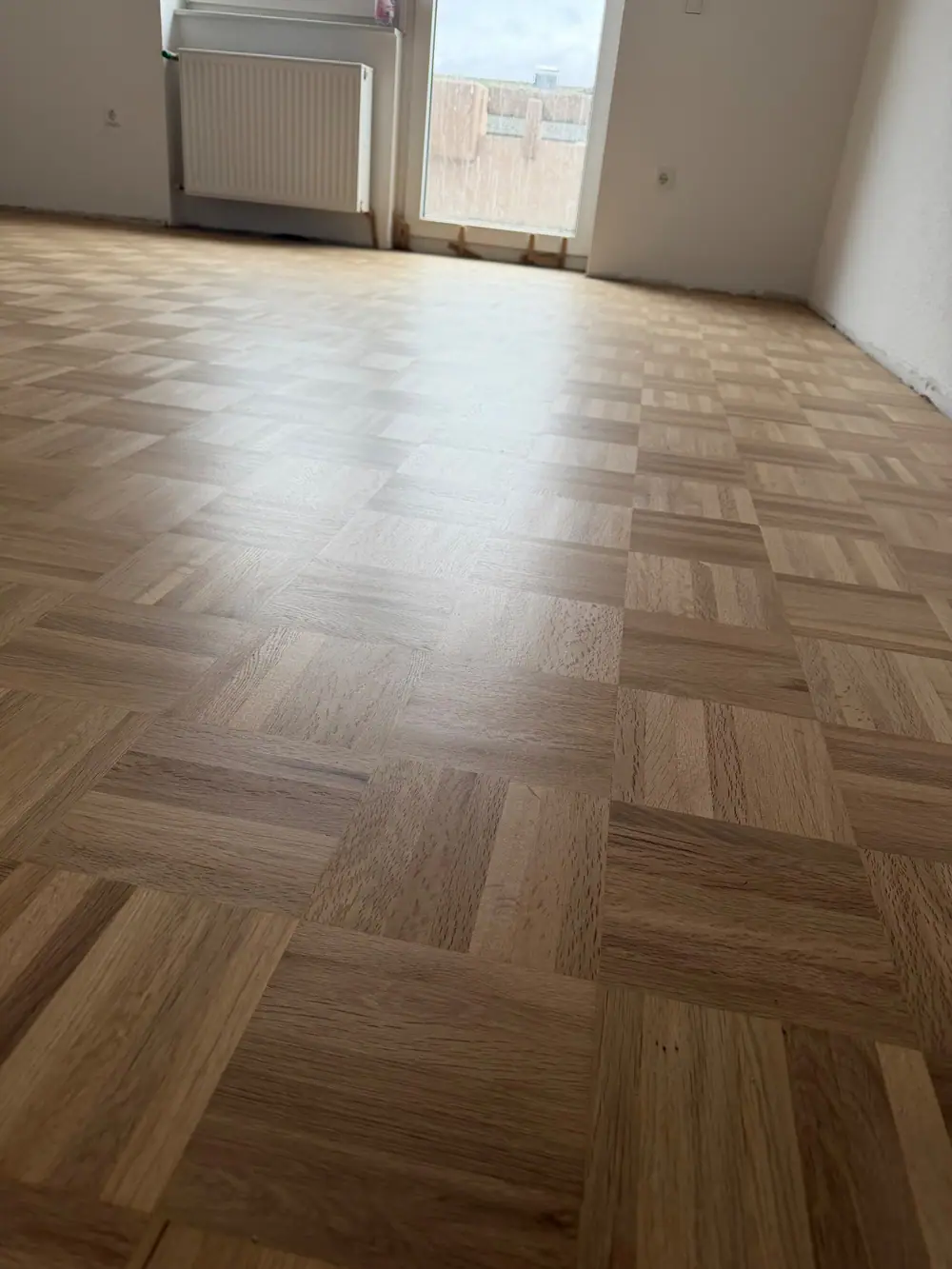 Bodennaher Blick über das sanierte Eiche-Mosaikparkett mit matt wirkender Oberfläche und deutlich sichtbarer Holzmaserung.