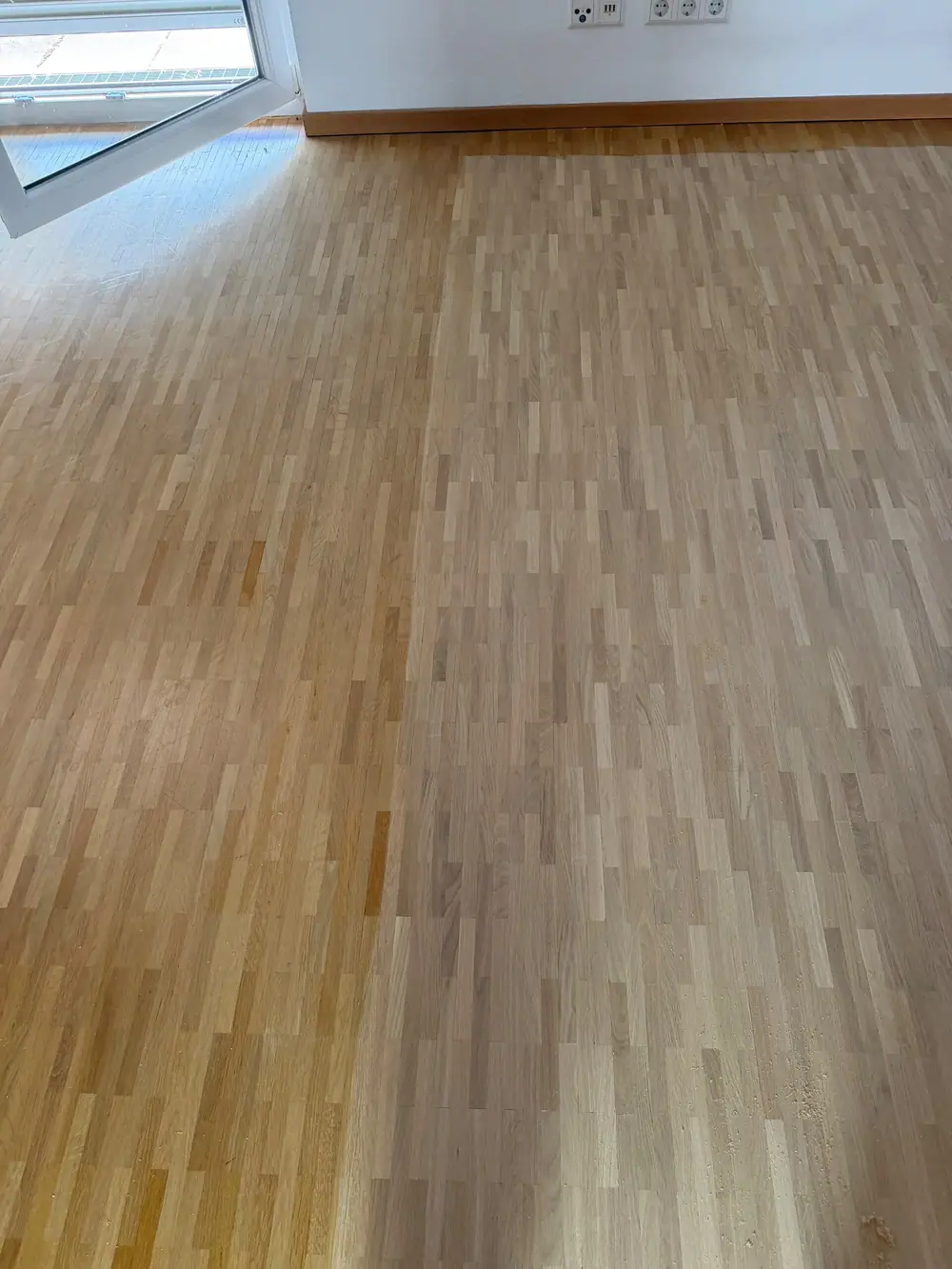 Nahansicht des geschliffenen Eichenparketts an einer geöffneten Balkontür mit Sockelleiste.