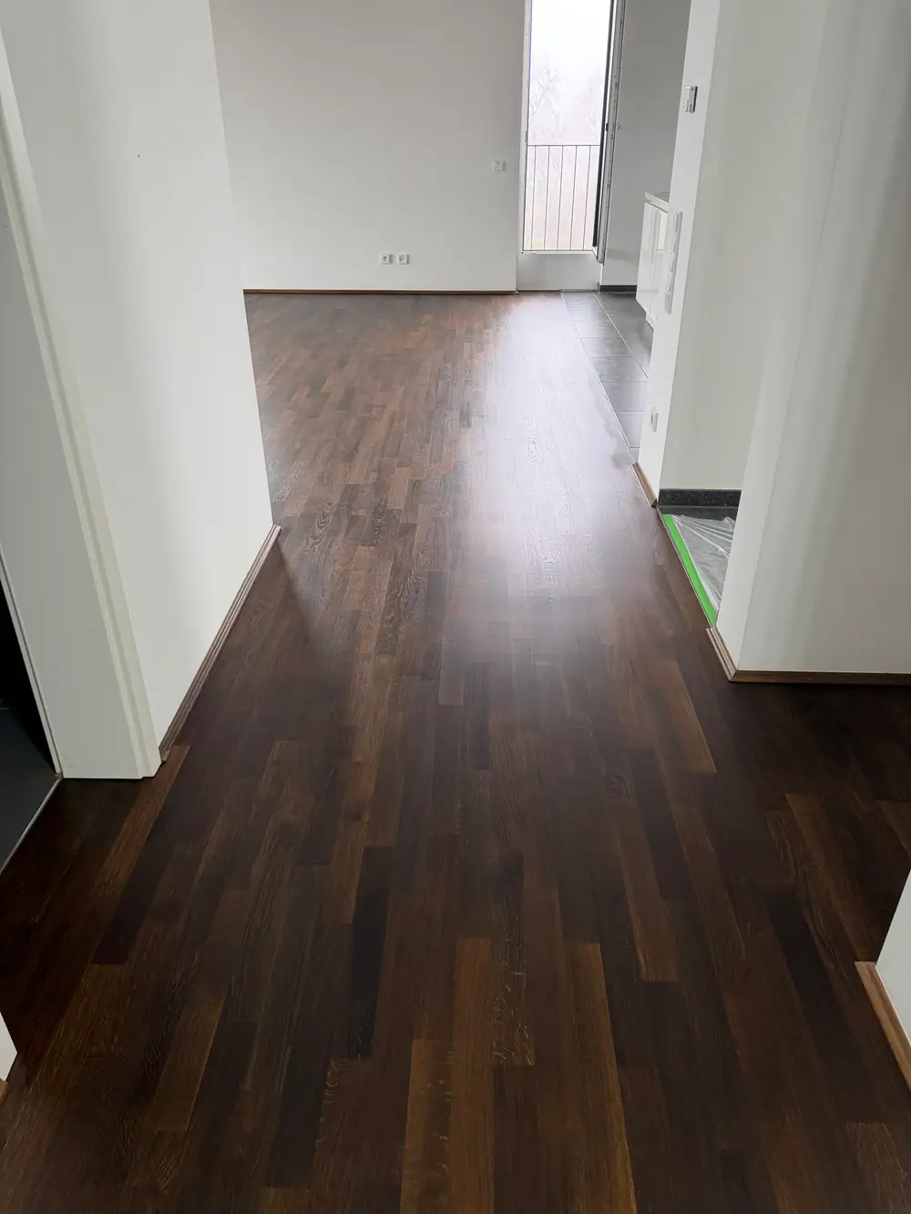 Dunkler Holzboden in einem hellen Durchgang mit weißen Wänden und Türöffnungen.