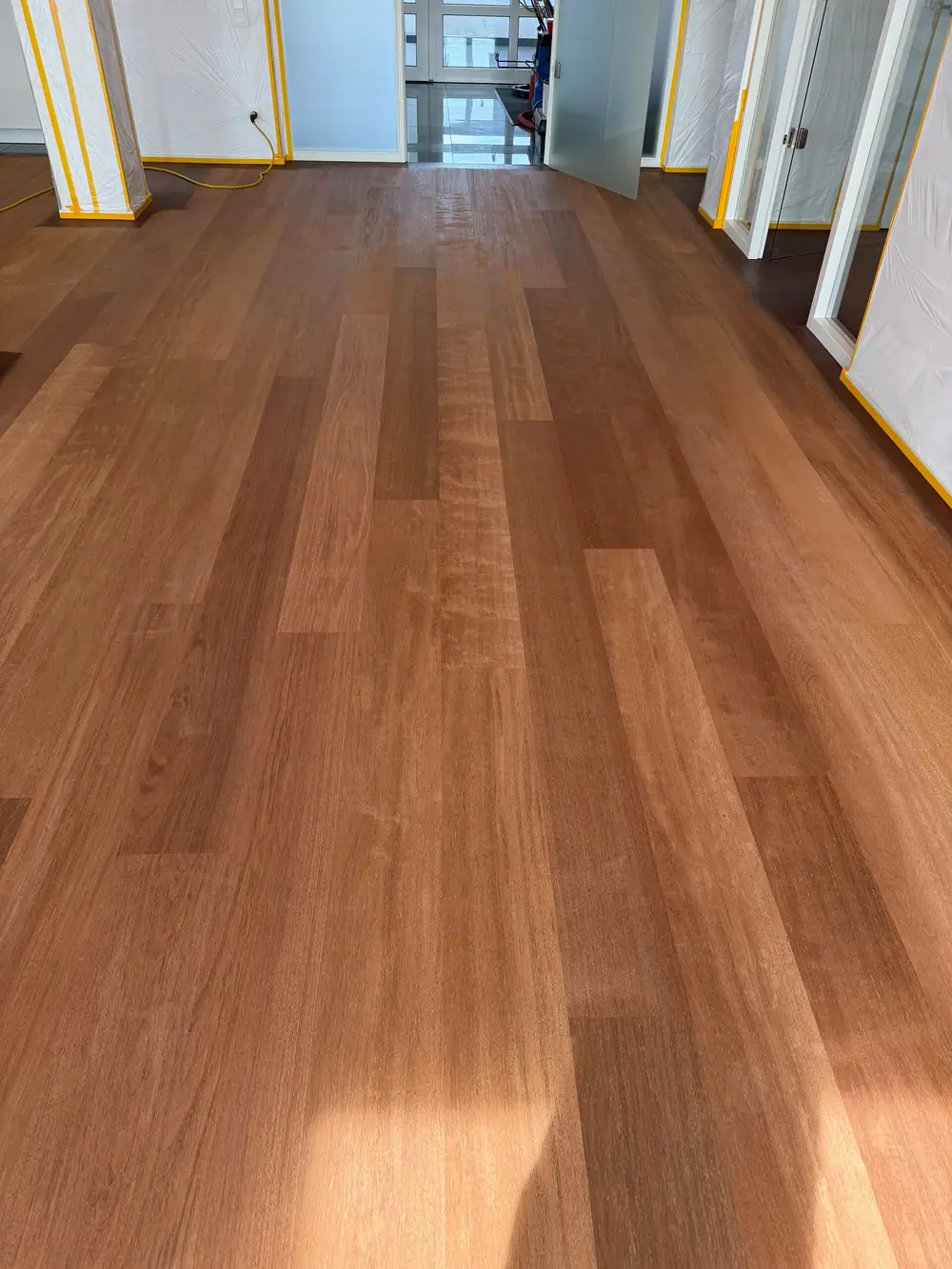 Nahansicht einer helleren bearbeiteten Landhausdielenfläche vor einer geöffneten Glastür und abgedeckten Wänden.