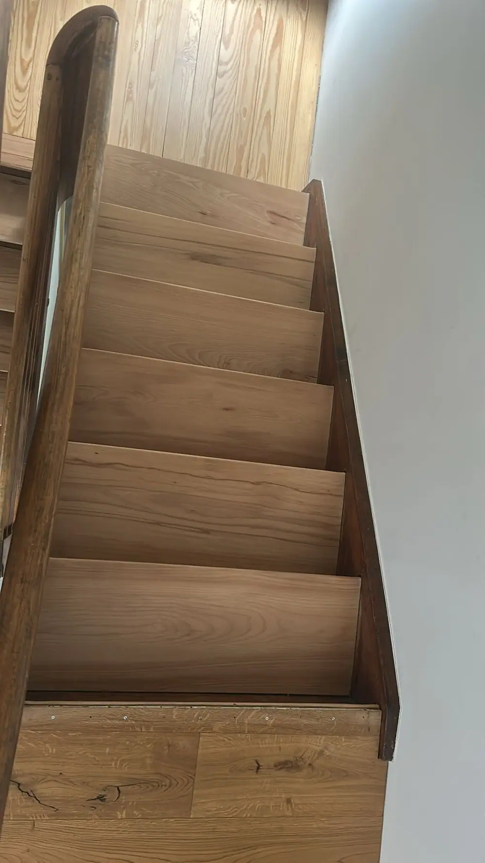 Ansicht eines Treppenlaufs mit Holzstufen, Holzhandlauf und dunkler seitlicher Abschlussleiste.