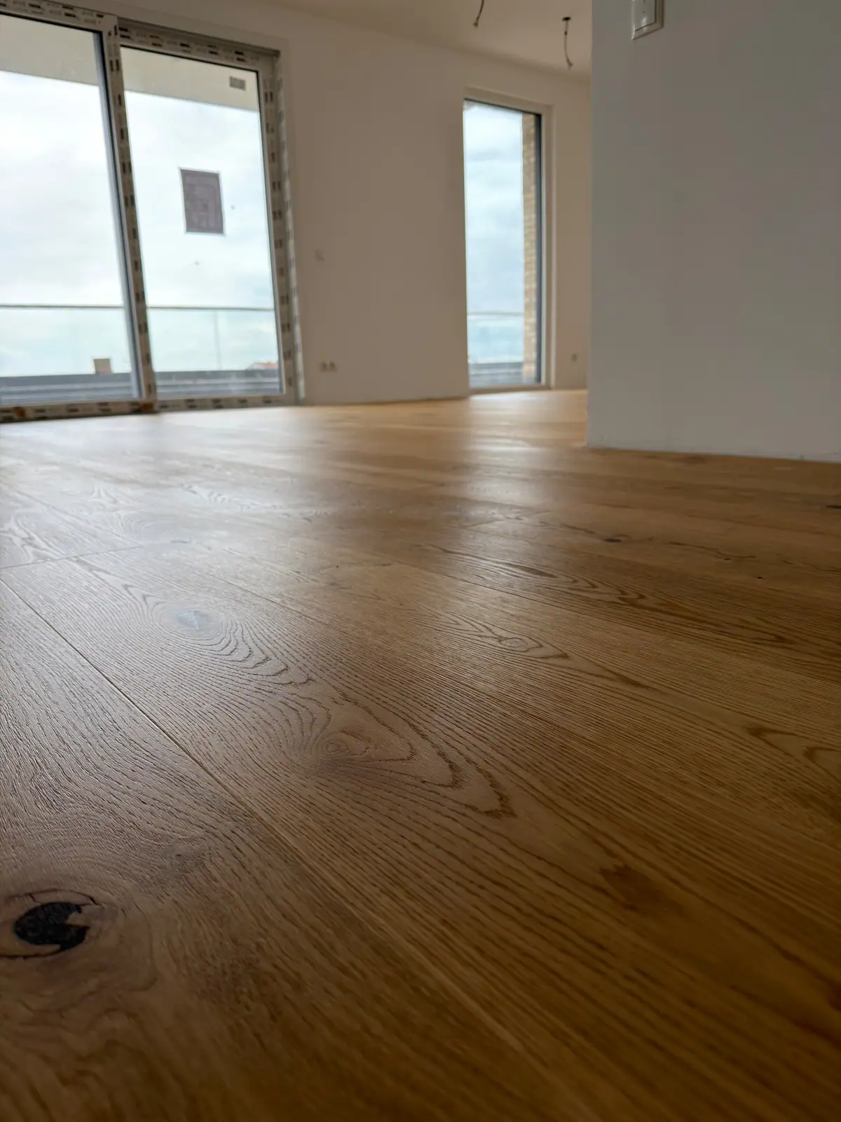 Bodennaher Blick auf die Eiche-Landhausdielen in einem hellen Raum mit großen Fenstern.