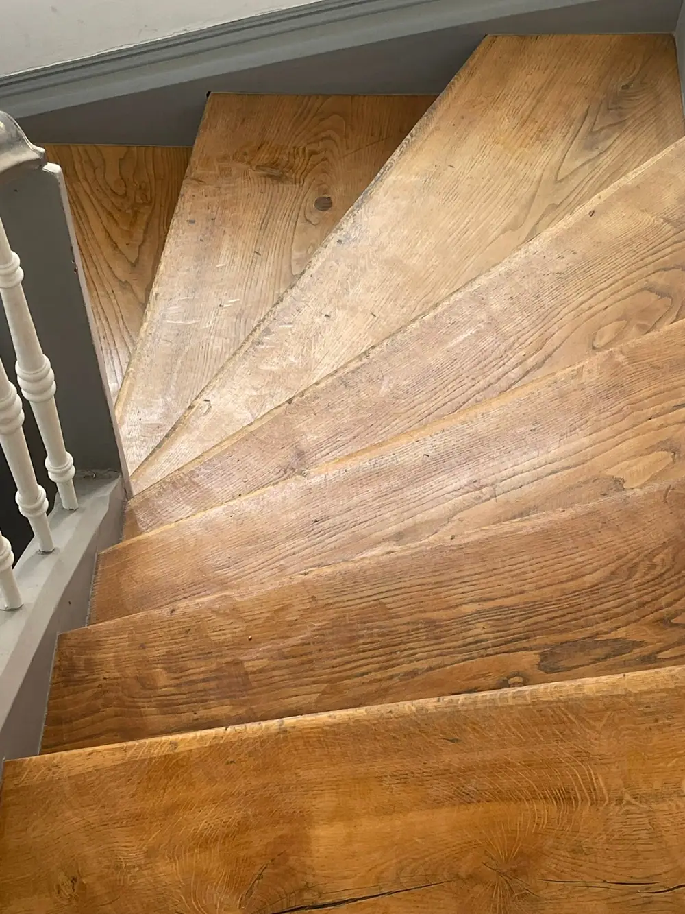 Blick auf dunklere, deutlich gebrauchte Holzstufen einer gewendelten Treppe mit sichtbaren Kratzern und Laufspuren.