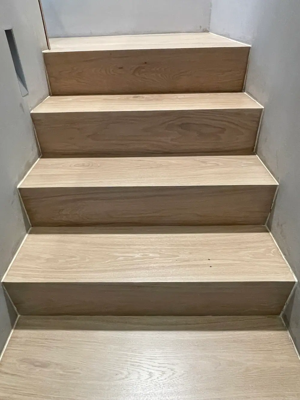 Gerade Holztreppe mit breiten Trittstufen und sichtbaren Setzstufen zwischen hellen Wänden.