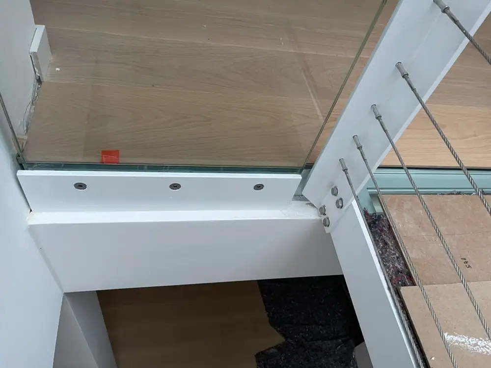 Glasgeländer mit Metallseilen über einer hellen Dielenfläche im Treppenbereich.