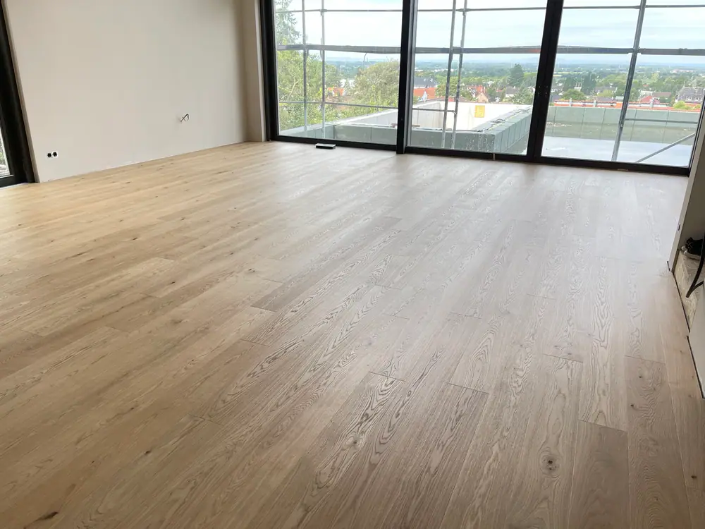 Heller Dielenboden in einem großen Raum mit bodentiefen Fenstern und sichtbarer Holzmaserung.