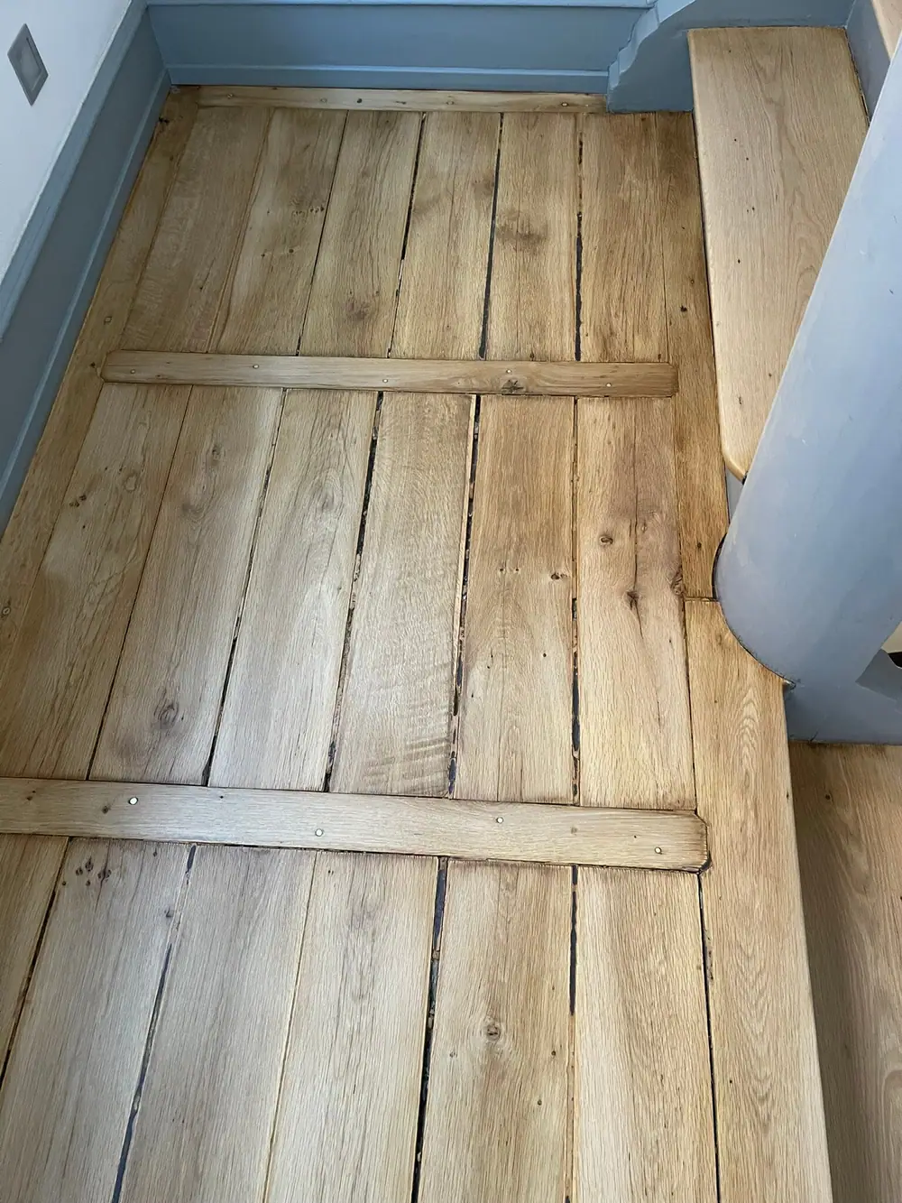 Draufsicht auf ein Treppenpodest aus breiten Holzdielen mit dunklen Fugen und quer verlaufenden Holzleisten.