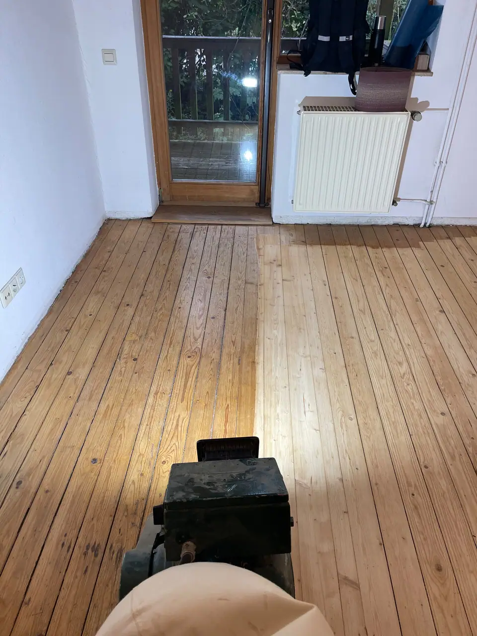 Holzdielen in einem Raum während der Schleifarbeit; im Vordergrund steht eine Schleifmaschine.
