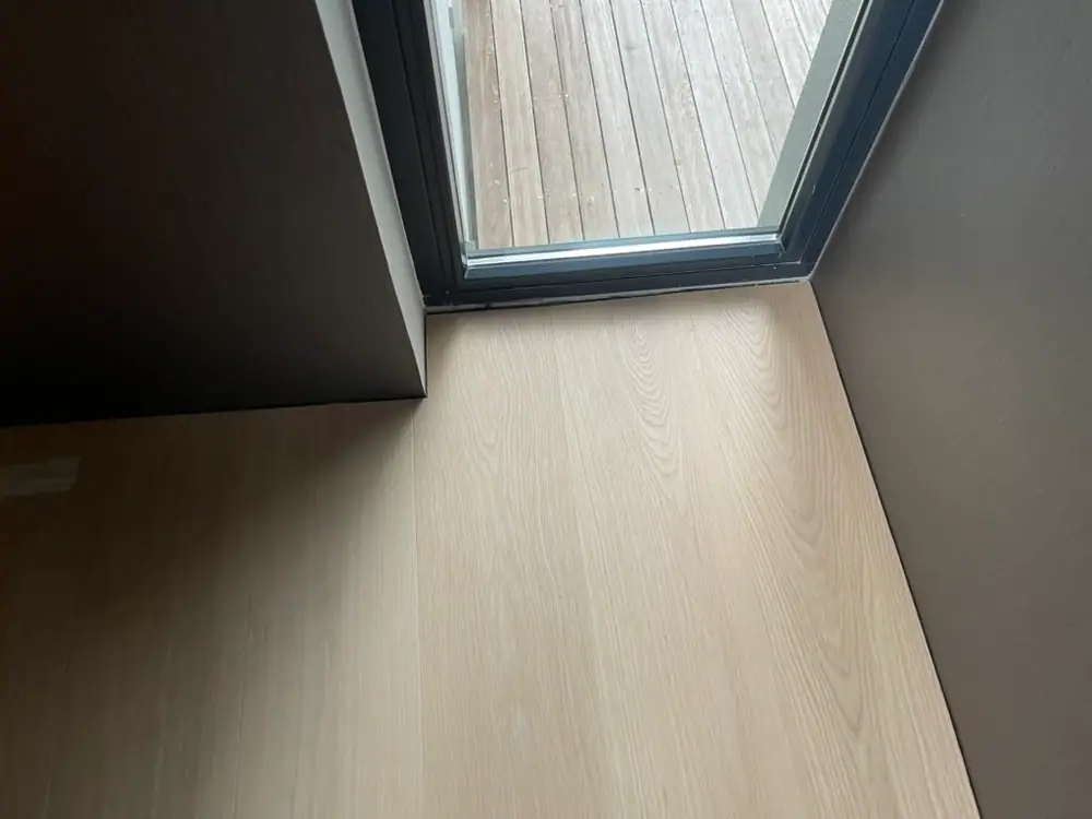 Helle Holzdiele mit präzisem Zuschnitt an einem dunklen Türrahmen.