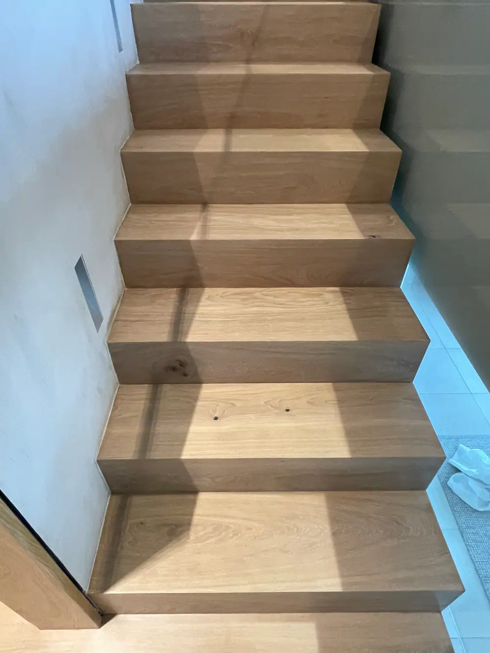 Holztreppe mit mehreren Stufen, auf denen Schatten einer Fensterkonstruktion liegen.