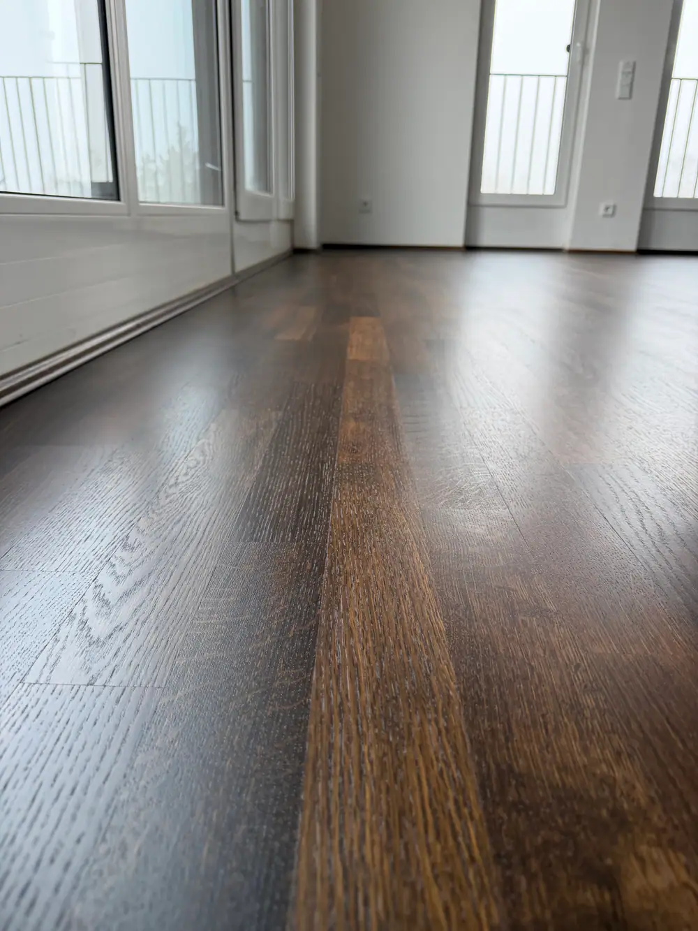Dunkler Holzboden am unteren Rahmen einer weißen Fenstertür.