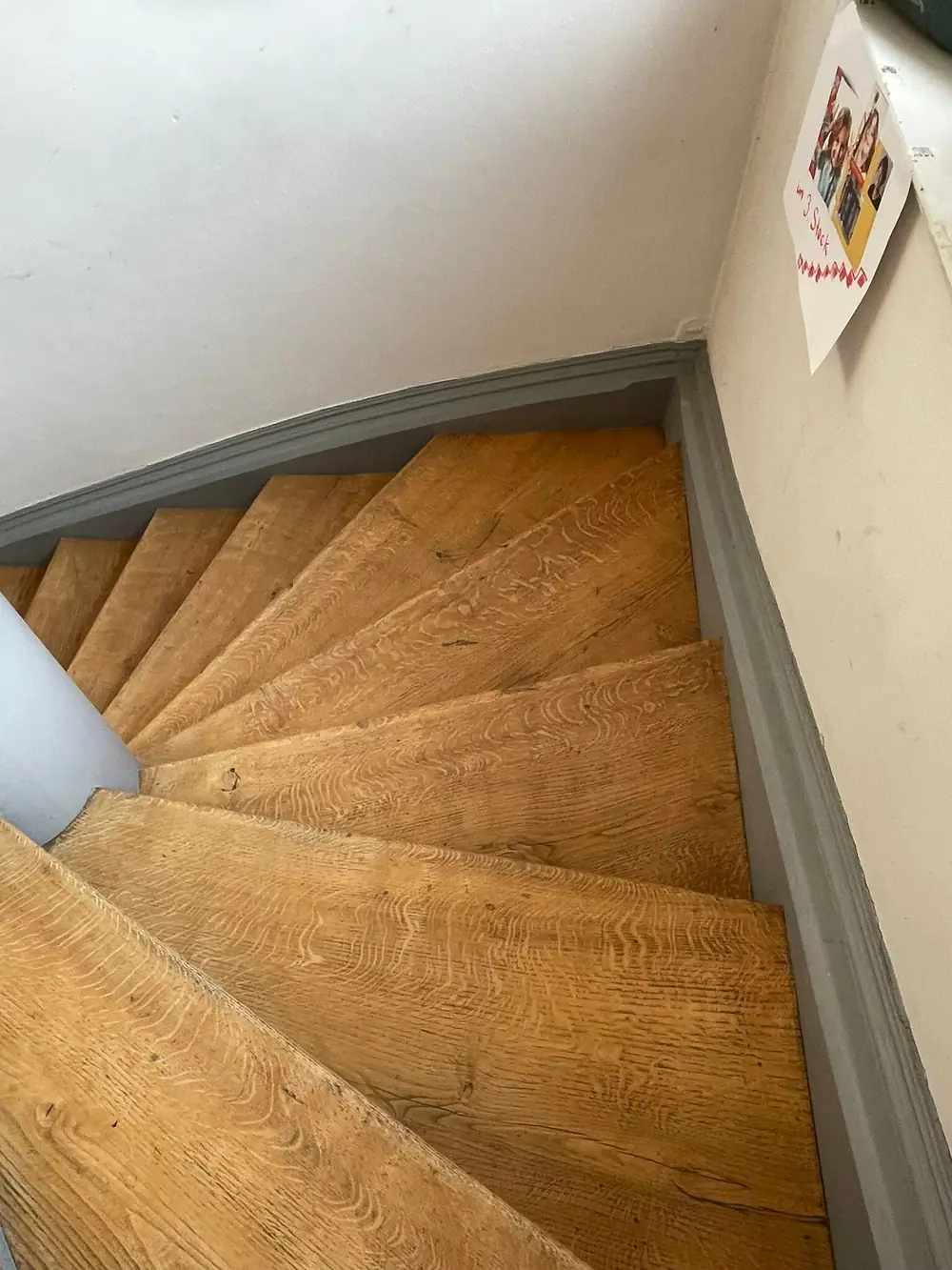 Blick von oben auf gewendelte Holzstufen entlang einer weißen Wand mit grauer Sockelleiste.
