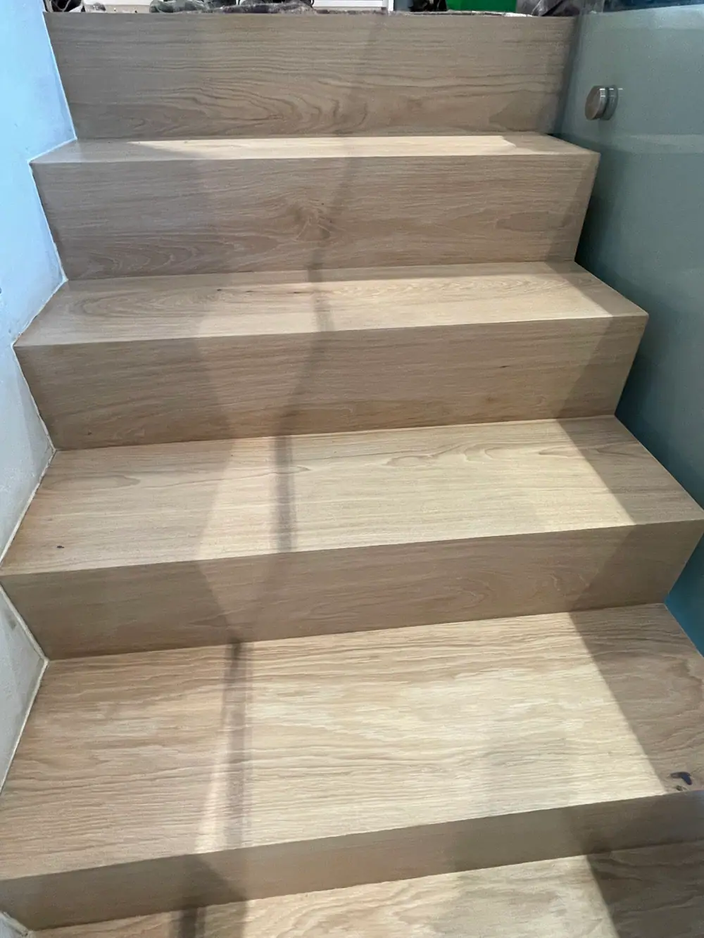 Blick auf eine Holztreppe mit breiten Stufen, sichtbarer Maserung und Licht-Schatten-Muster.