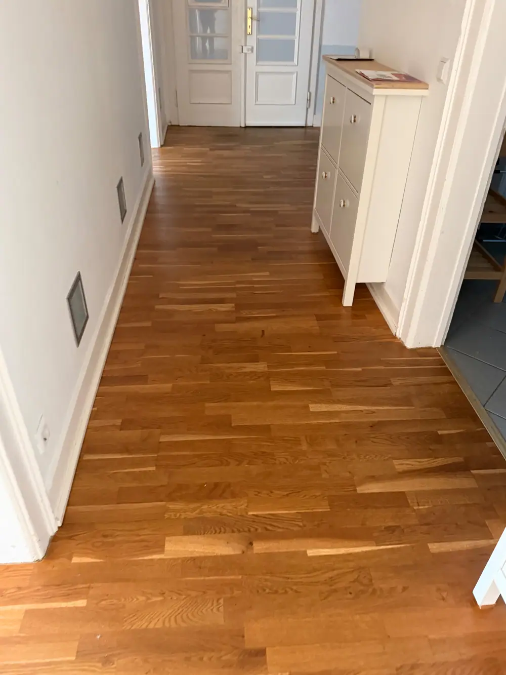 Blick durch einen Innenraum mit geölten Landhausdielen, weißen Einbauten und Fenstern.