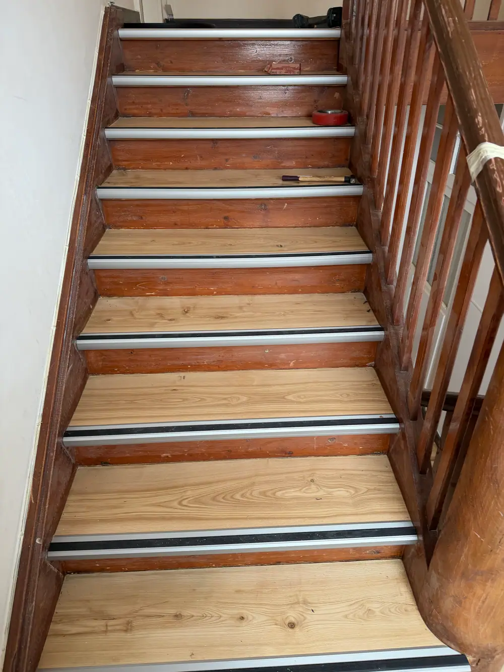 Blick auf einen Treppenlauf mit hellen Holztrittflächen, dunklem Holzgeländer sowie Aluminiumprofilen mit schwarzen Gummieinlagen.