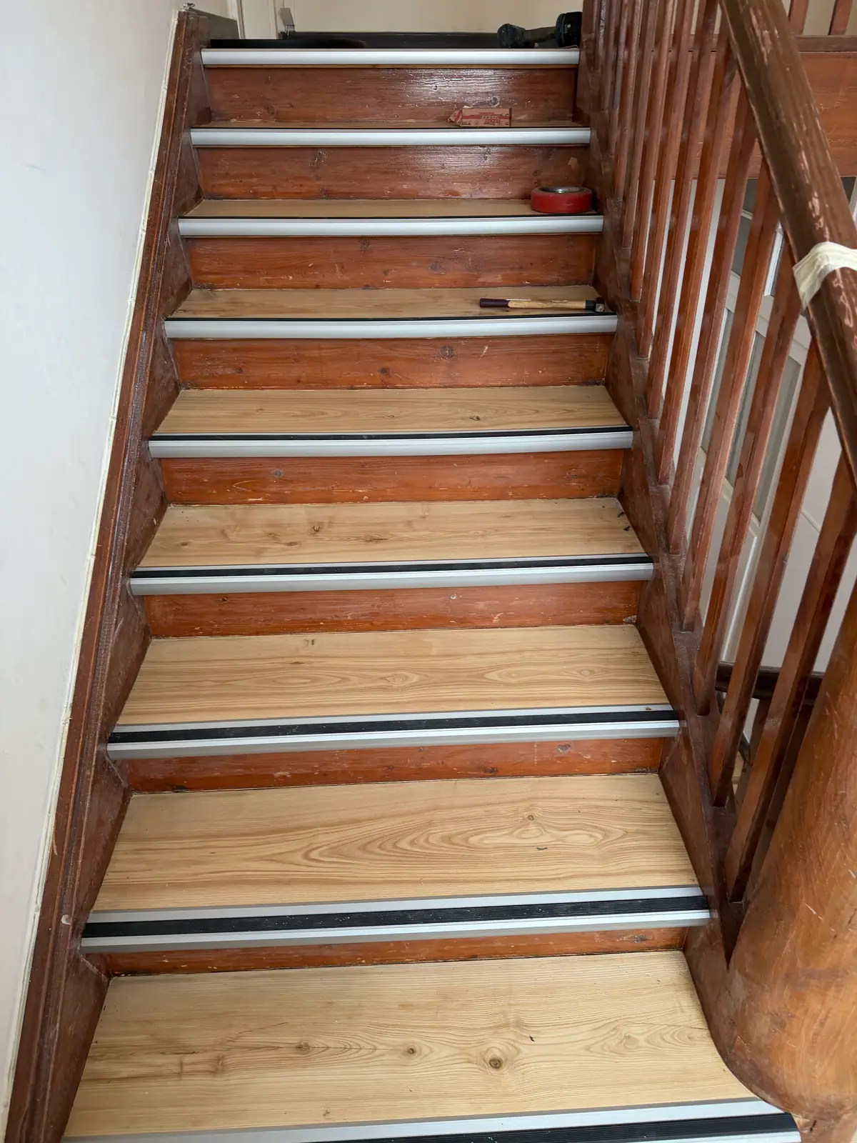 Blick auf einen Treppenlauf mit hellen Holztrittflächen, dunklem Holzgeländer sowie Aluminiumprofilen mit schwarzen Gummieinlagen.