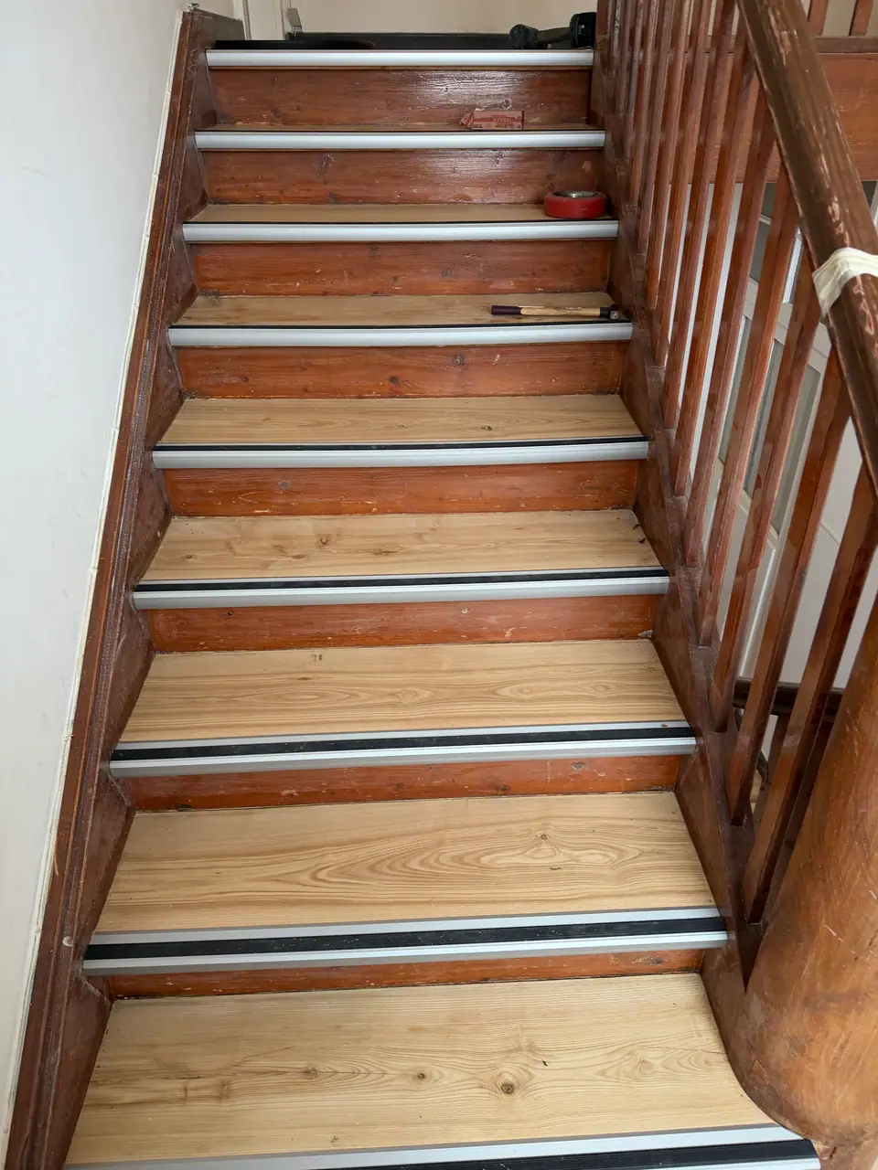 Blick auf einen Treppenlauf mit hellen Holztrittflächen, dunklem Holzgeländer sowie Aluminiumprofilen mit schwarzen Gummieinlagen.