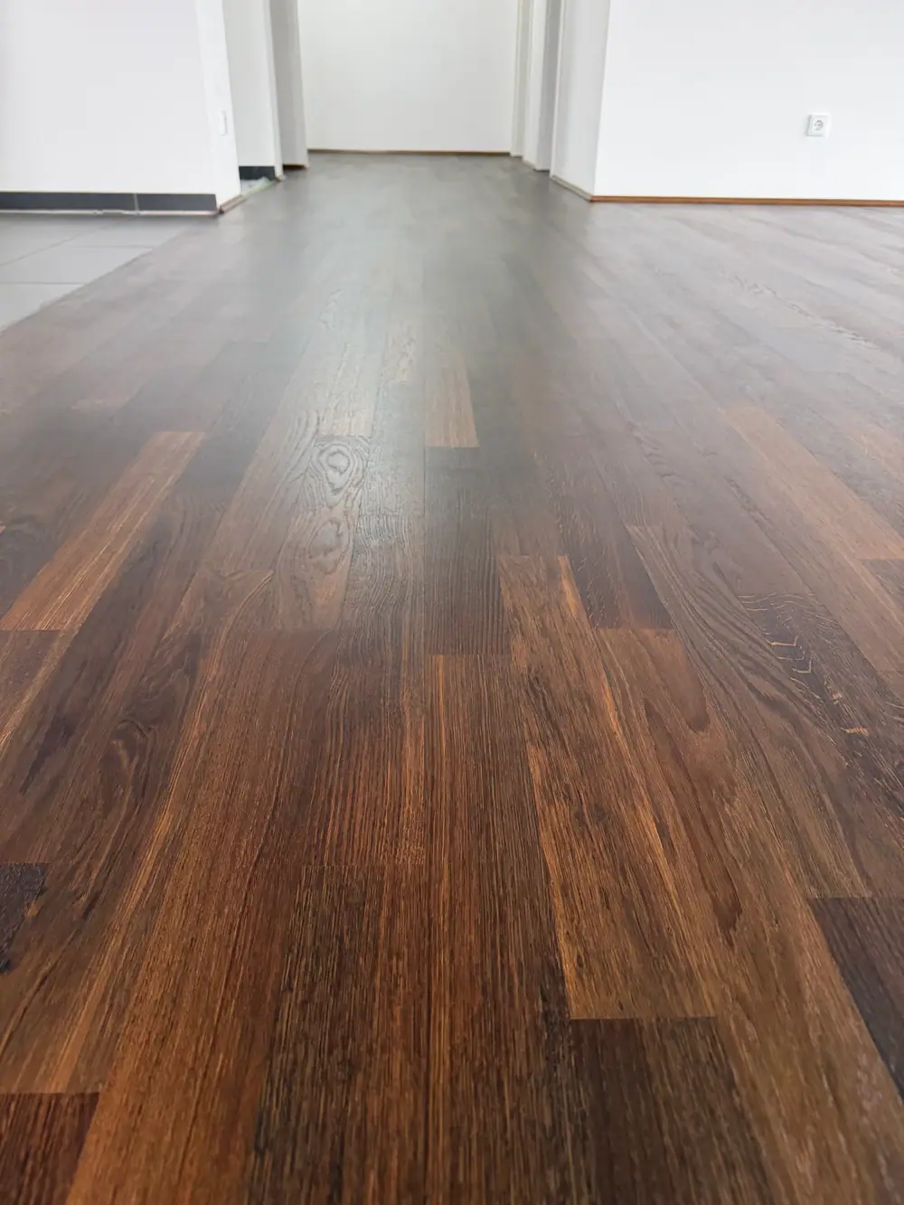Nahaufnahme eines dunklen Holzbodens mit sichtbarer Maserung und unterschiedlichen Brauntönen.