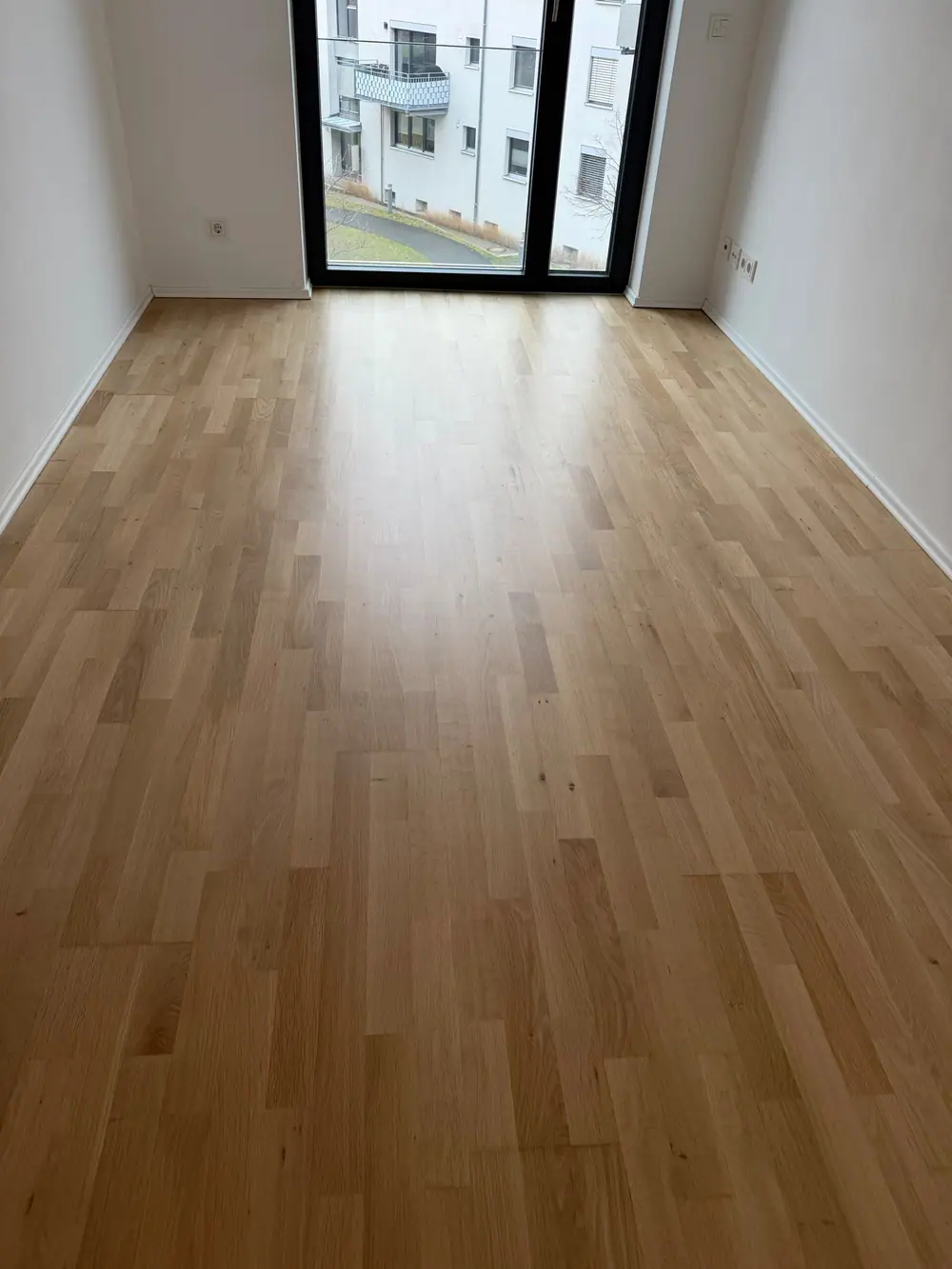 Schmaler leerer Raum mit Eiche-Parkett und bodentiefer Fensterfront.