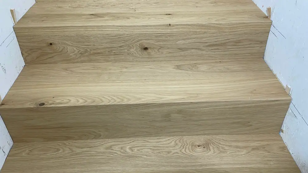Ansicht mehrerer breiter Holzstufen mit Aststellen und ausgeprägter Holzmaserung.